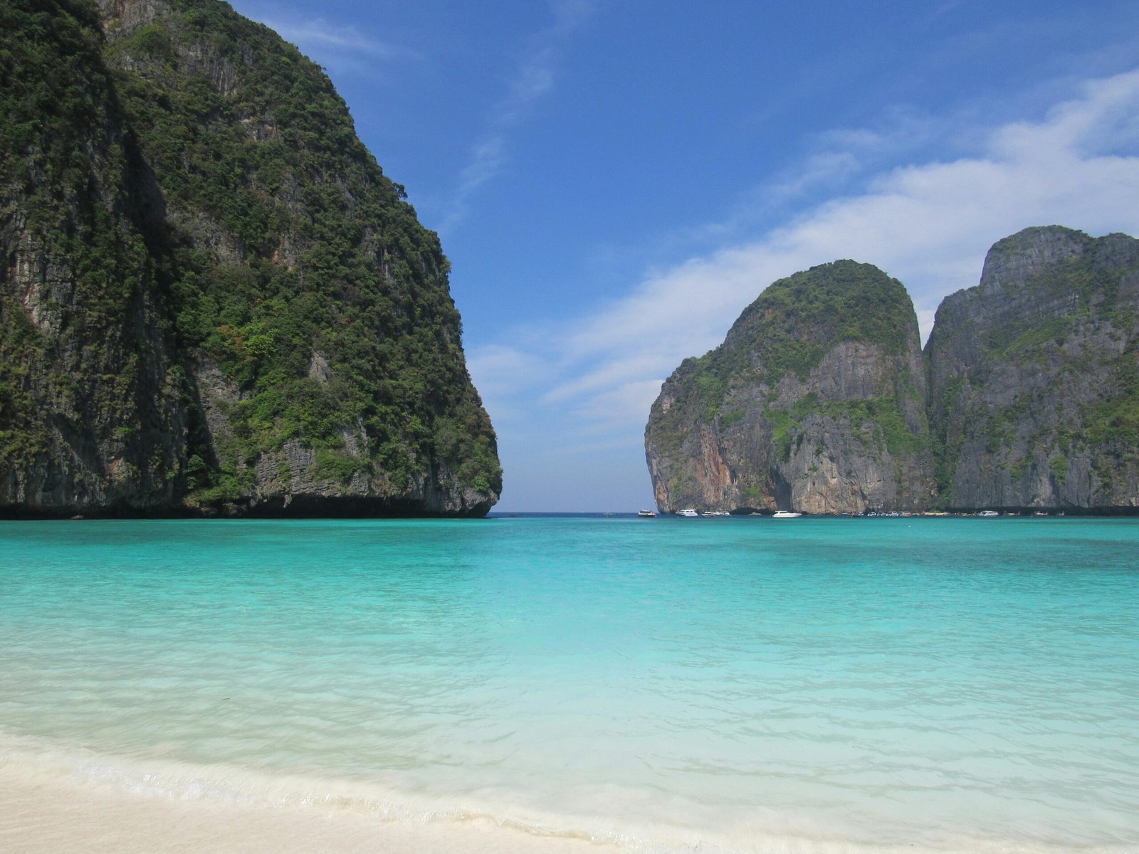 Tranquil tropical beach in Thailand featuring clear turquoise waters and lush cliffs.