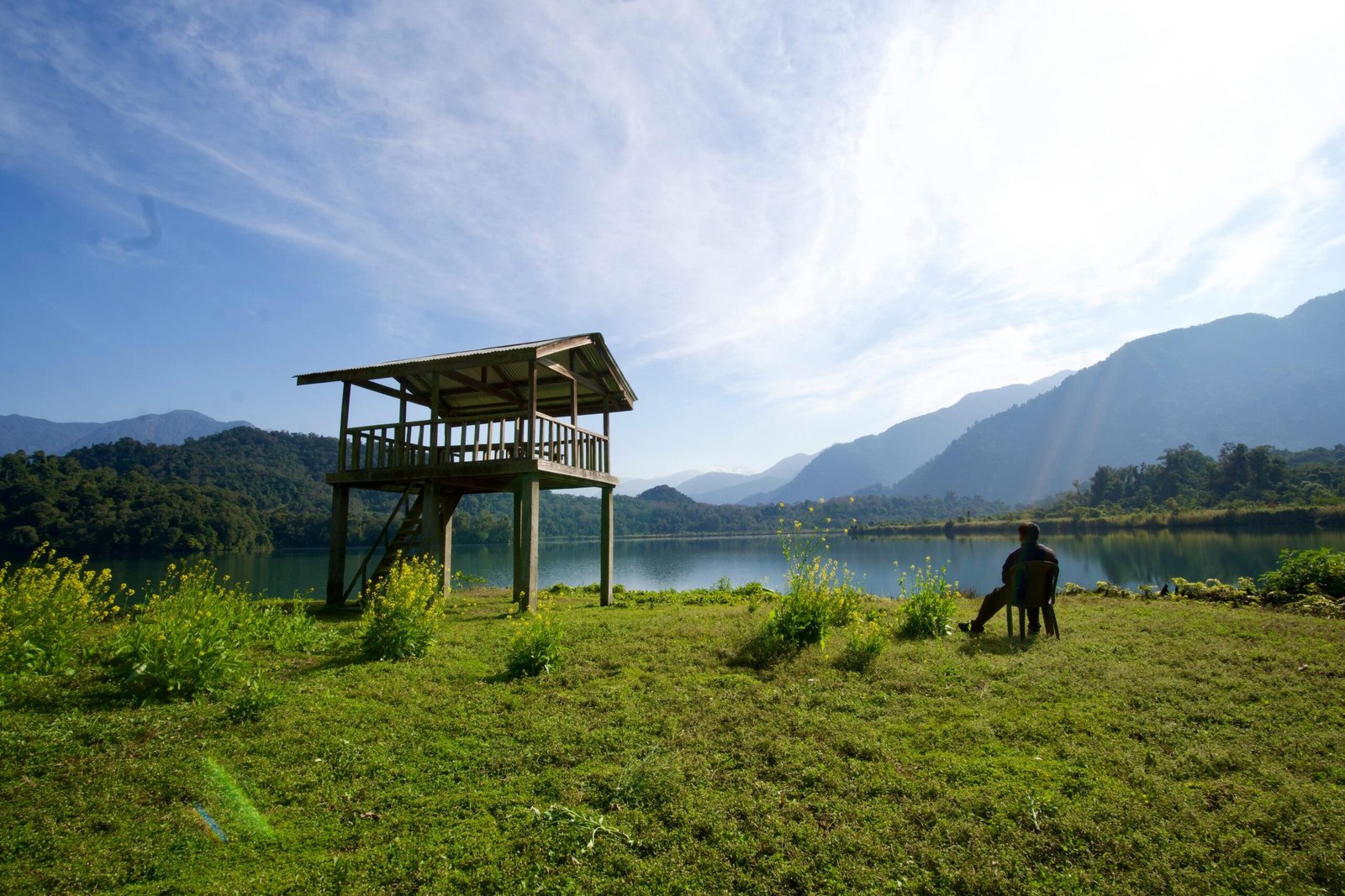 A serene scene with a man relaxing by a lake under a clear sky and observation tower.