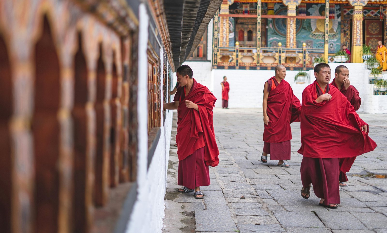 Buddhist monks in red robes walking and interacting in a Bhutan temple courtyard.